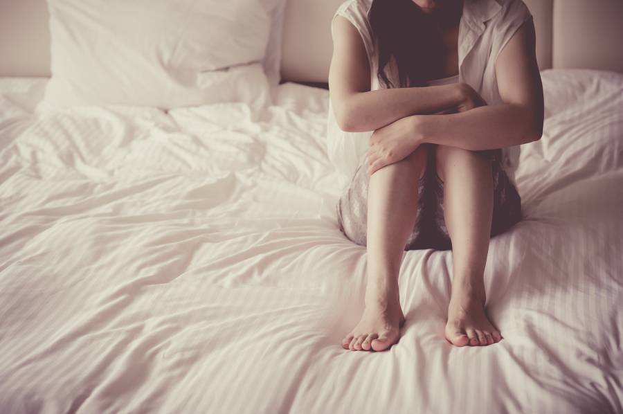 ベッドの上で膝を抱えて座る女性